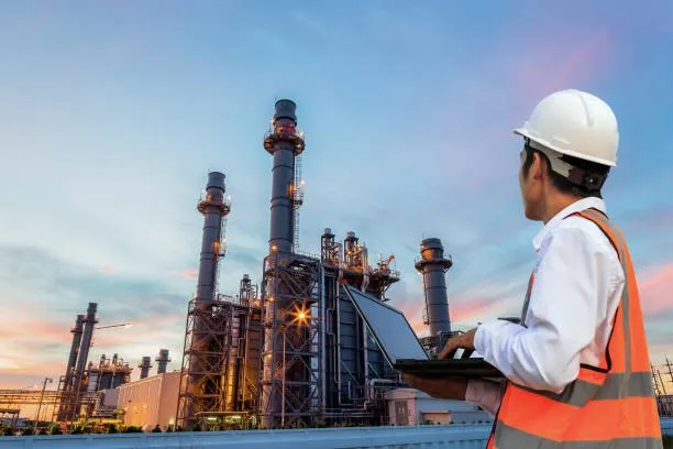 Worker with laptop at an oil refinery.